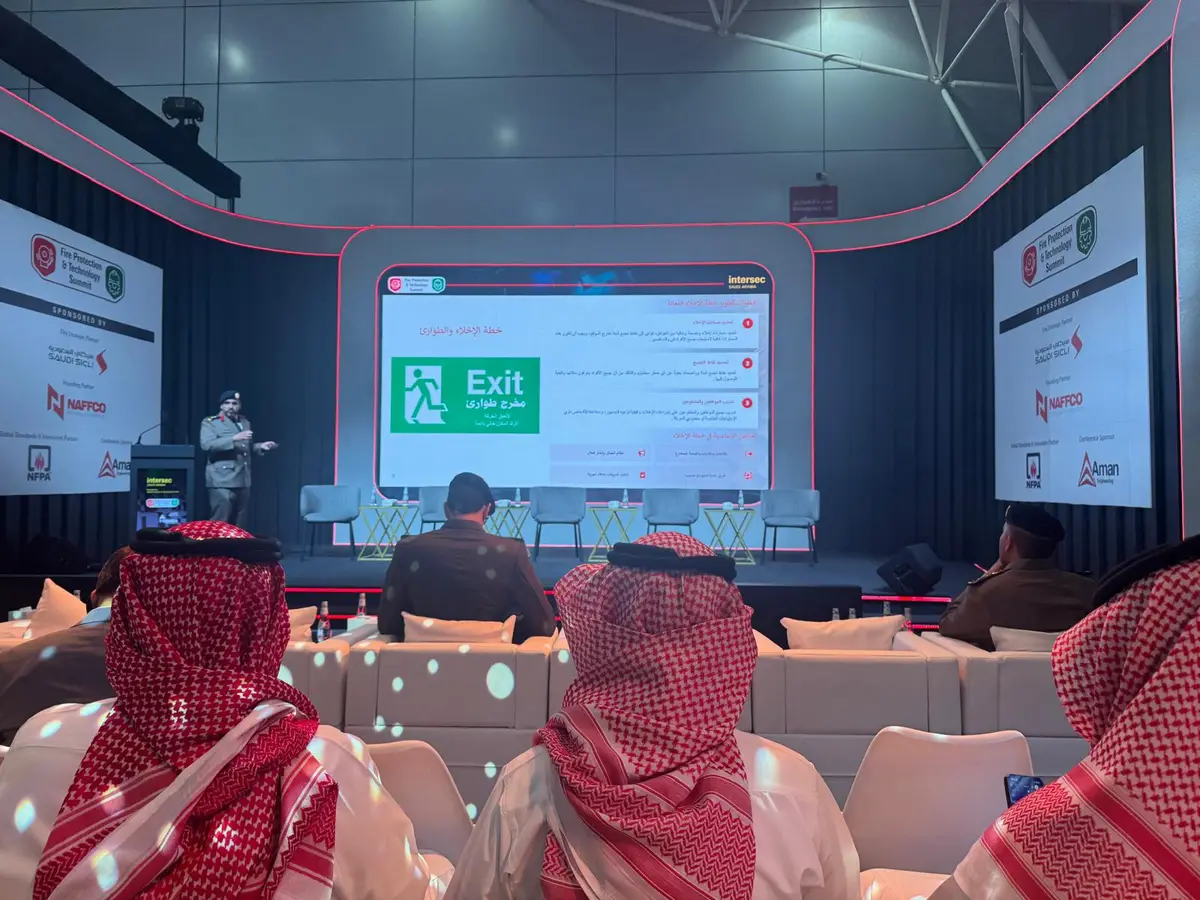 Delegates seated in a conference auditorium at a fire protection and technology summit, watching a presentation on evacuation and emergency planning shown in Arabic and English.